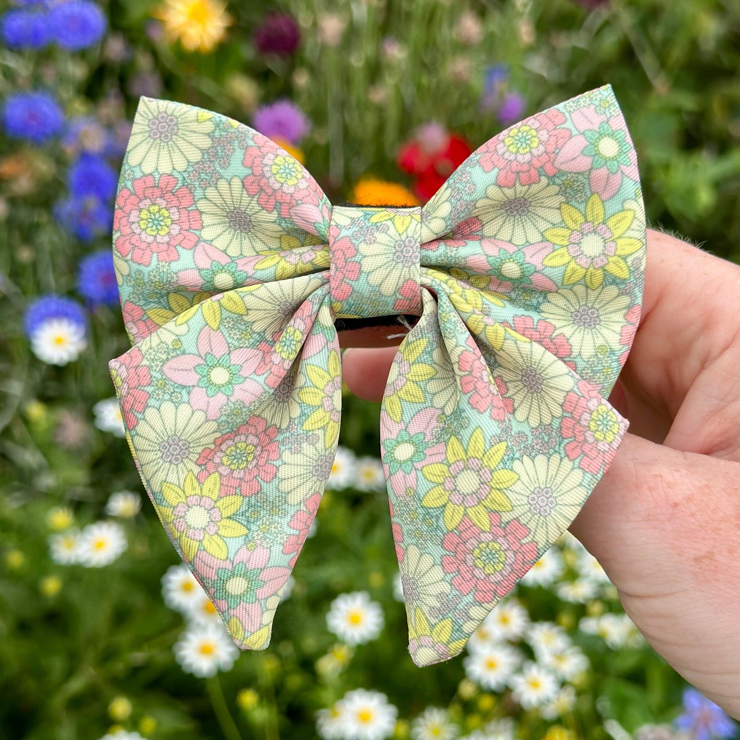 Floral-patterned hair bow held in front of a field of flowers