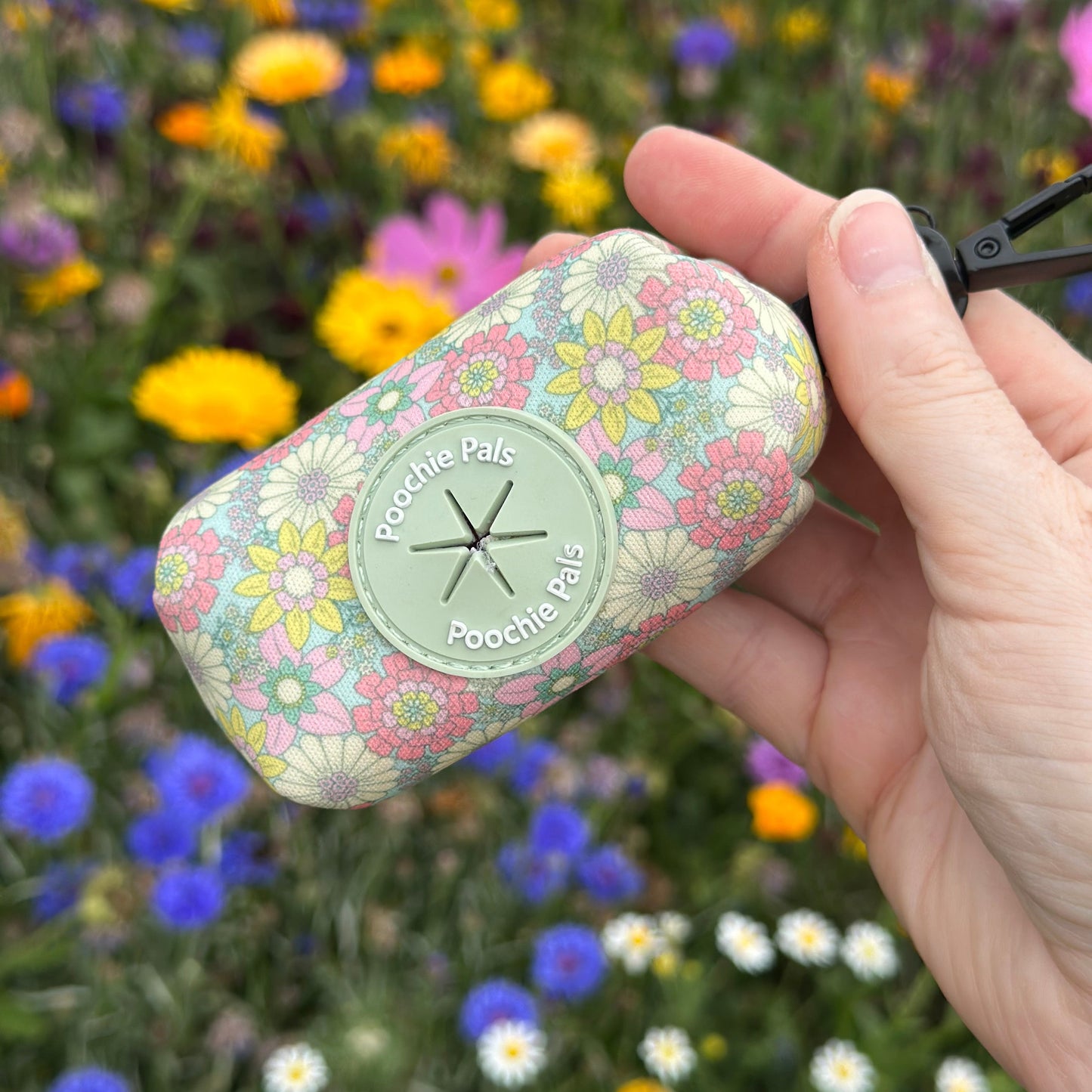 Hand holding a floral-patterned product with a blurred flower background